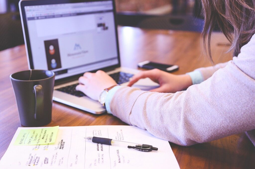 mujer tecleando en una laptop con cuadernos y apuntes